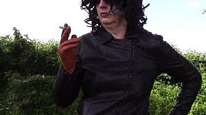 She smokes while wearing cinnamon leather trousers outdoors.