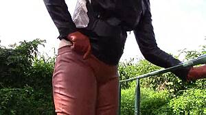 She smokes while wearing cinnamon leather trousers outdoors.